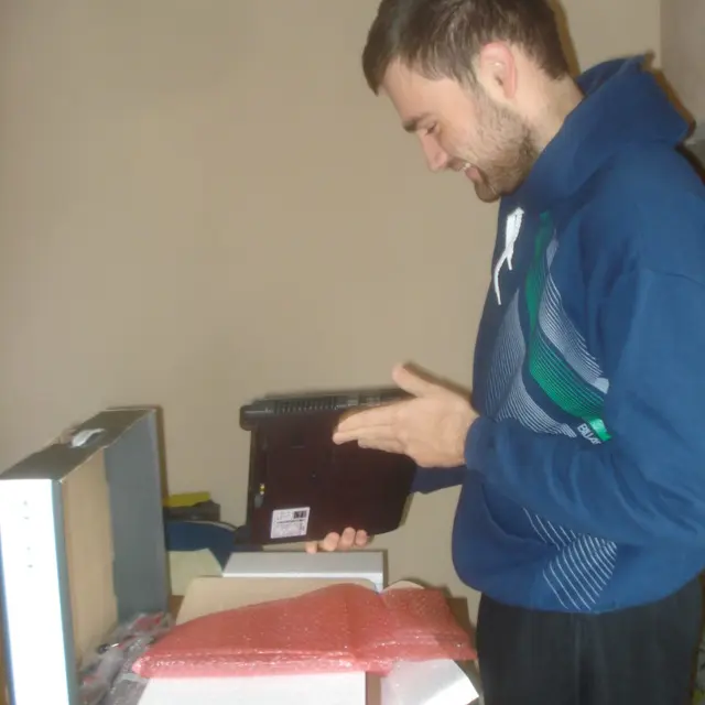 Chico sonriendo, sacando del envoltorio una laptop nueva