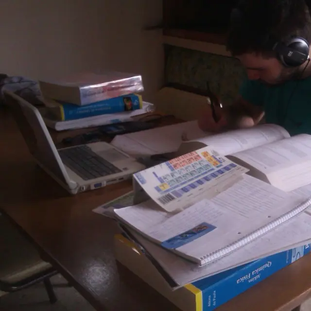 Chico estudiando química rodeado de materiales y una computadora portátil